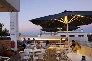 A rooftop dining area with tables and chairs, umbrellas, and a view of a boat in the background. - Tiny Whale Lodge, a unique space for groups (Lagos)