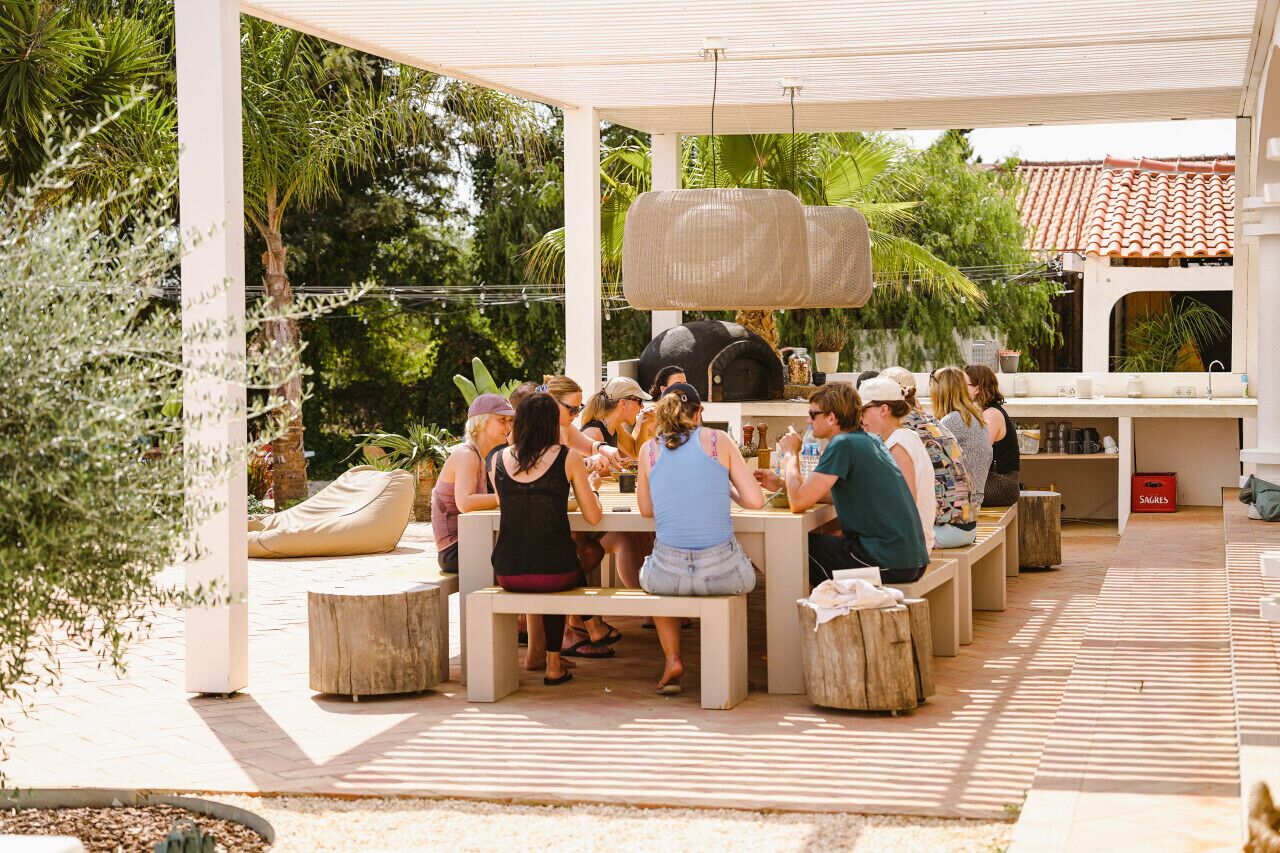 An outdoor patio with people seated at tables, surrounded by greenery and a pergola structure.