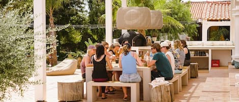An outdoor patio with people seated at tables, surrounded by greenery and a pergola structure.