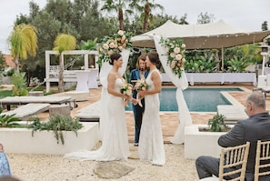 An outdoor wedding ceremony with a pool and lounge chairs in the background.