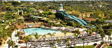 A resort with a large pool, multiple water slides, and a beach area with sun loungers.