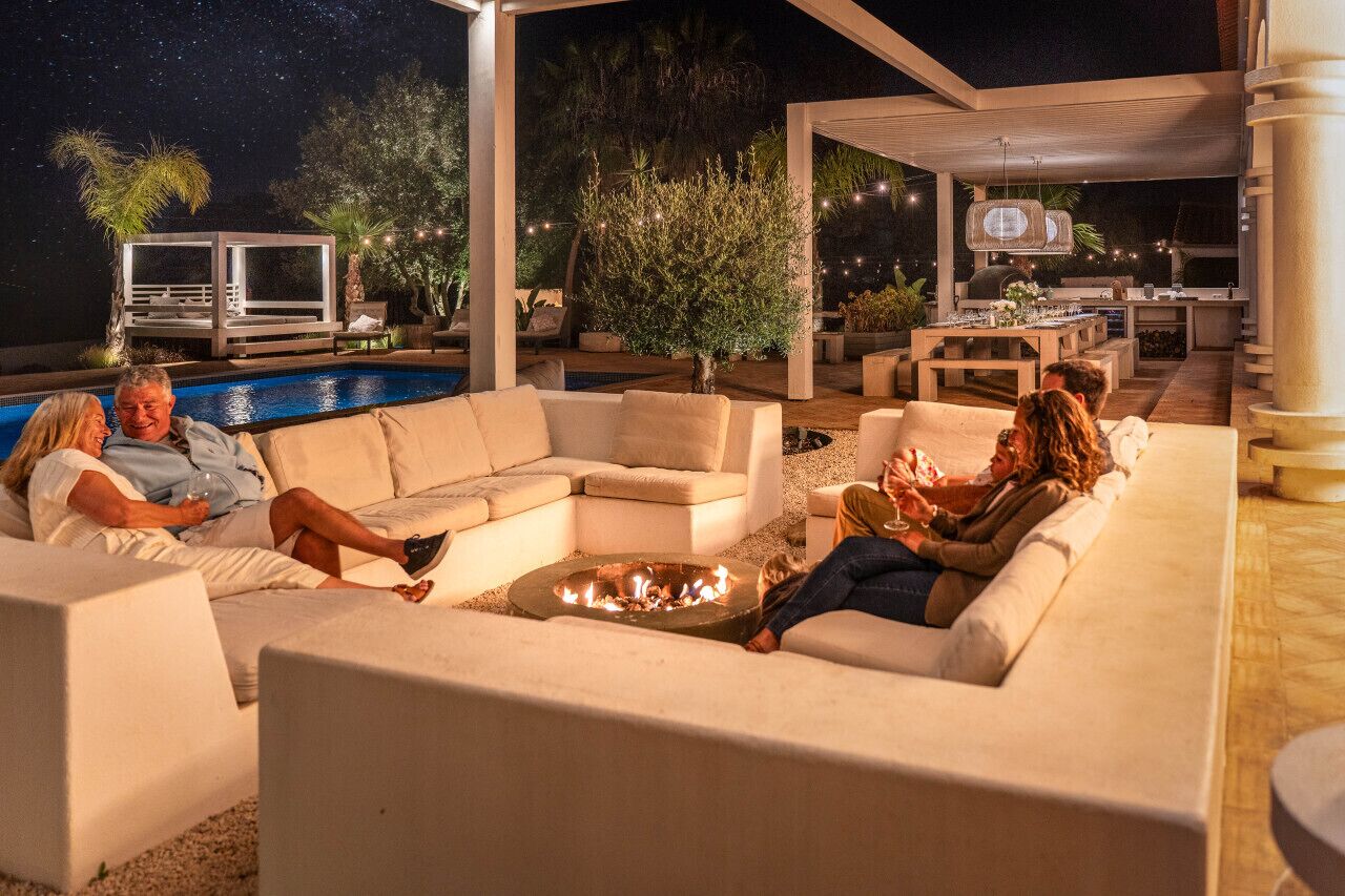 Uma área de estar coberta ao ar livre com piscina, lareira e churrasqueira.