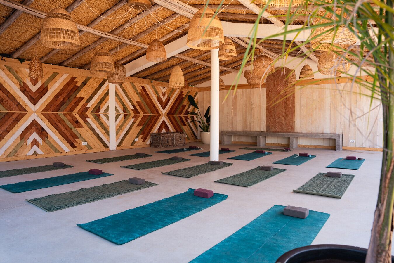 A yoga studio with wooden walls, tatami mats, and hanging rattan lamps.