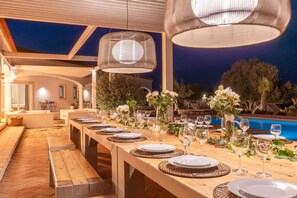 An outdoor dining area with a long wooden table set for a meal, surrounded by wicker chairs and equipped with wine glasses and plates. - Tiny Whale Lodge, a unique space for groups (Lagos)