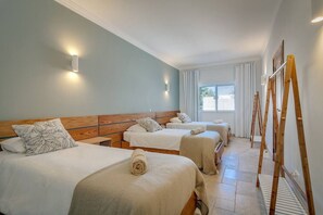 A hotel room with three beds, a wooden headboard, a window with curtains, and a wooden ladder. - Tiny Whale Lodge, a unique space for groups (Lagos)