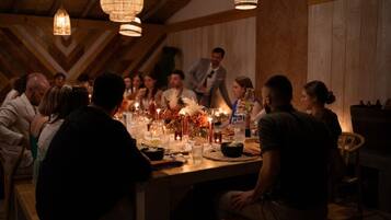 A group of people seated around a wooden table with candles and drinks, in a room with wooden walls and hanging lights.