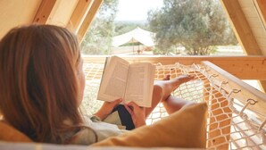 A person reading a book in a hammock with a view of trees and a tent in the background. - The Eden Lodge, a unique space for groups (Lagos)