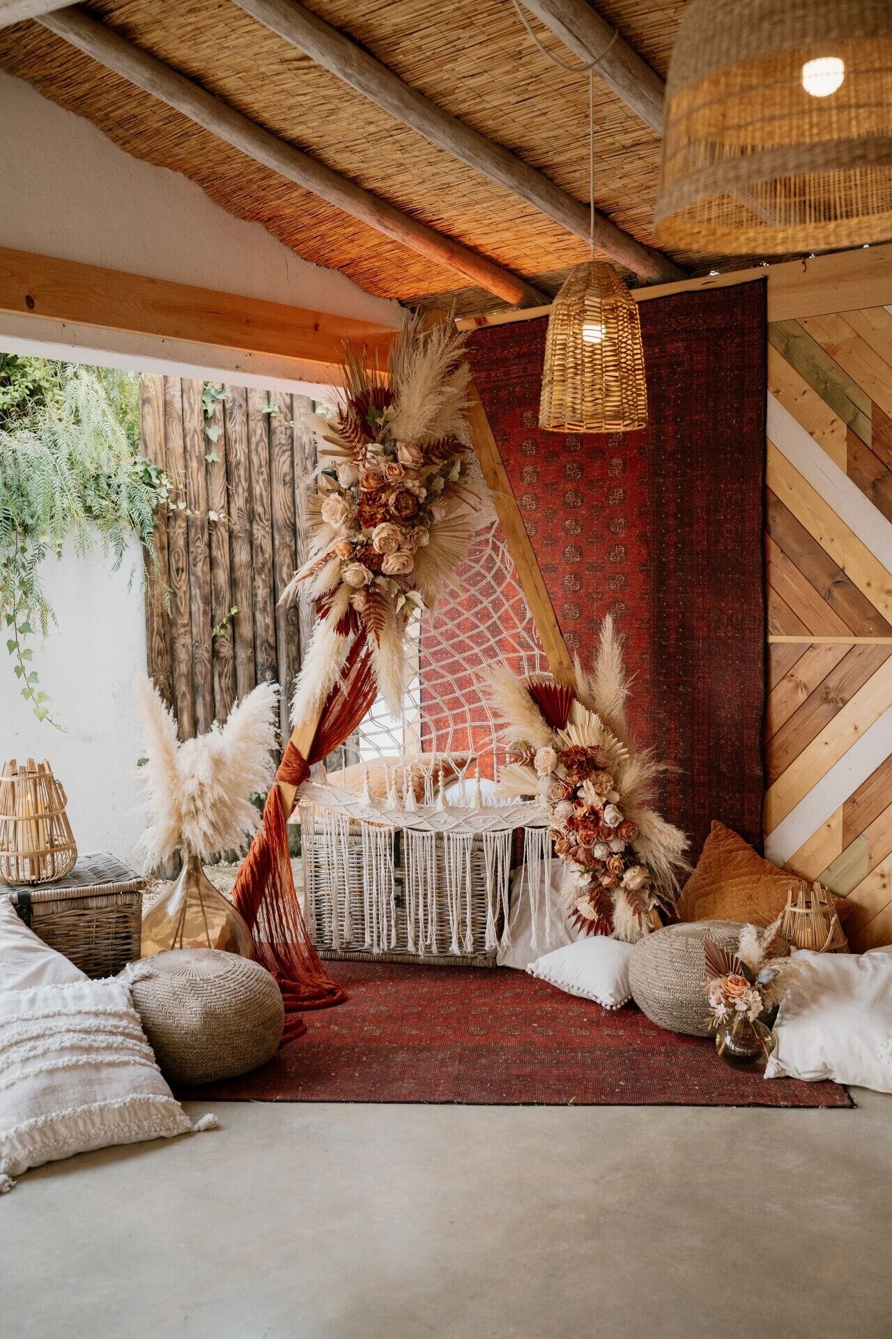 Un interior rústico con techo tejido, pared de diseño rojo y un arreglo decorativo de flores y plumas.