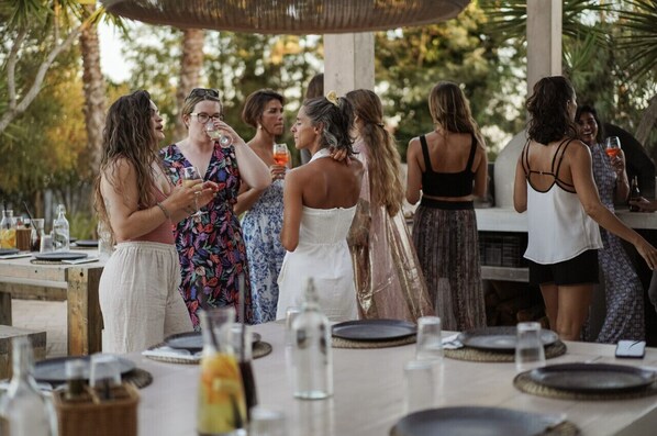 A group of people at an outdoor dining area with tables set for a meal.