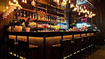 Zona de bar con diversos arreglos de asientos, estanterías llenas de botellas y lámparas colgantes.