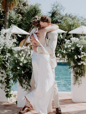 A couple embracing in front of a pool with white floral arrangements and umbrellas. - Tiny Whale Lodge, a unique space for groups (Lagos)