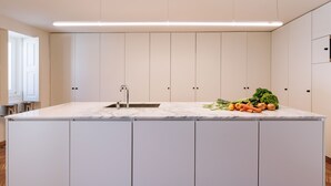 A modern kitchen with a marble countertop, a sink, and cabinets. There are vegetables on the countertop. - Travassos 11 (Elvas)