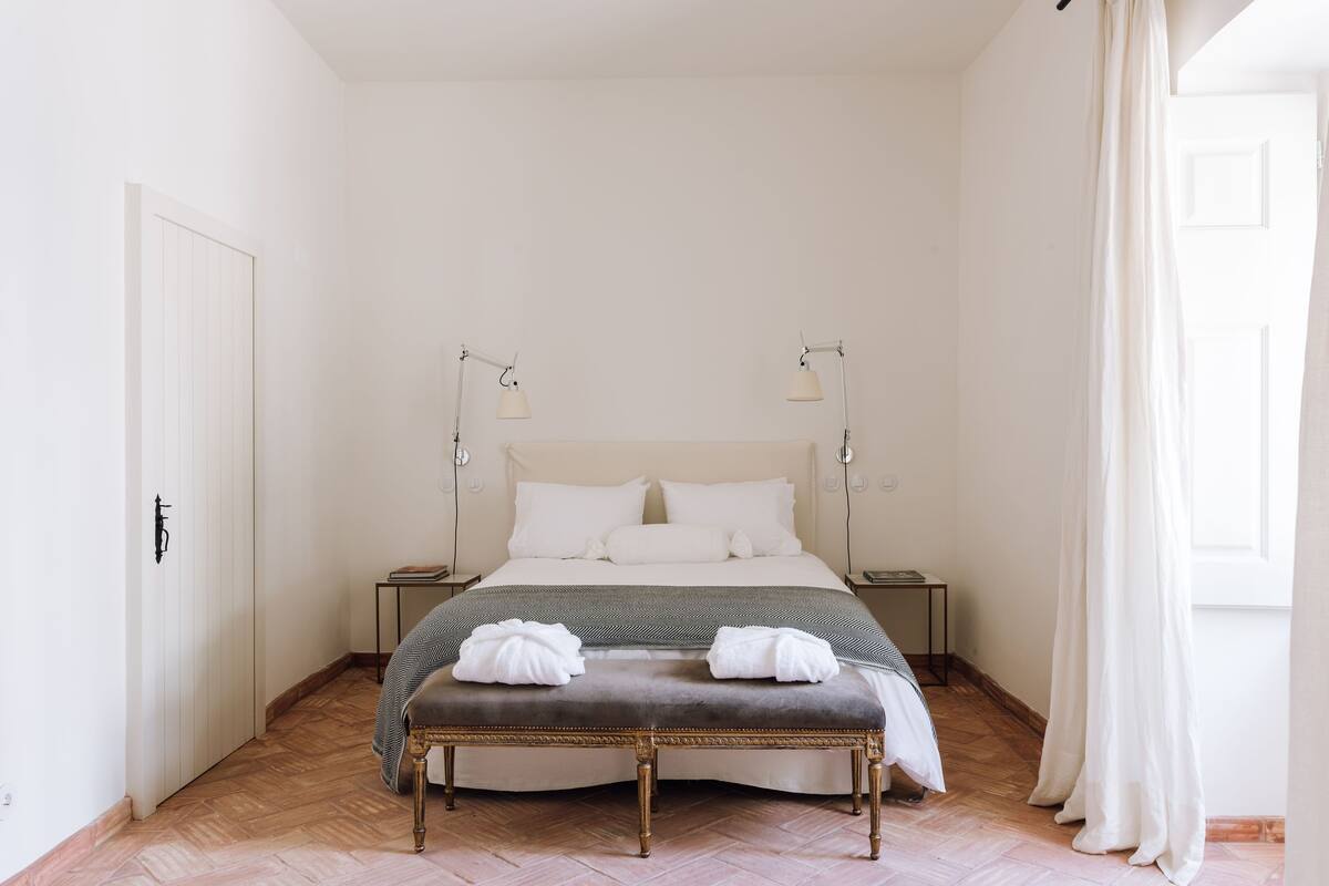 A neatly arranged bedroom with a bed, bedside tables, a bench, and a door.