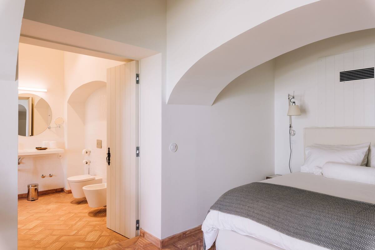 A bedroom with a bed, a bedside lamp, and a view of the bathroom.