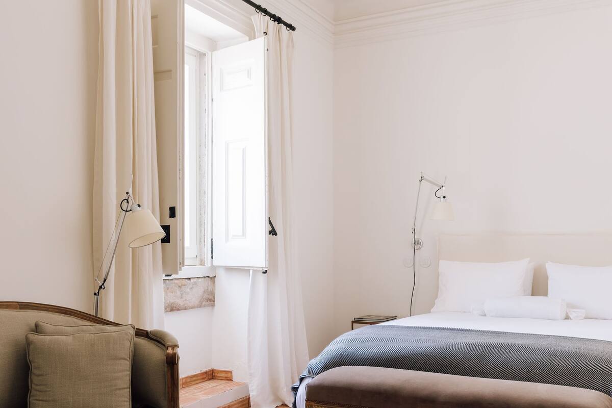 A bedroom with a bed, bench, lamp, and curtains.