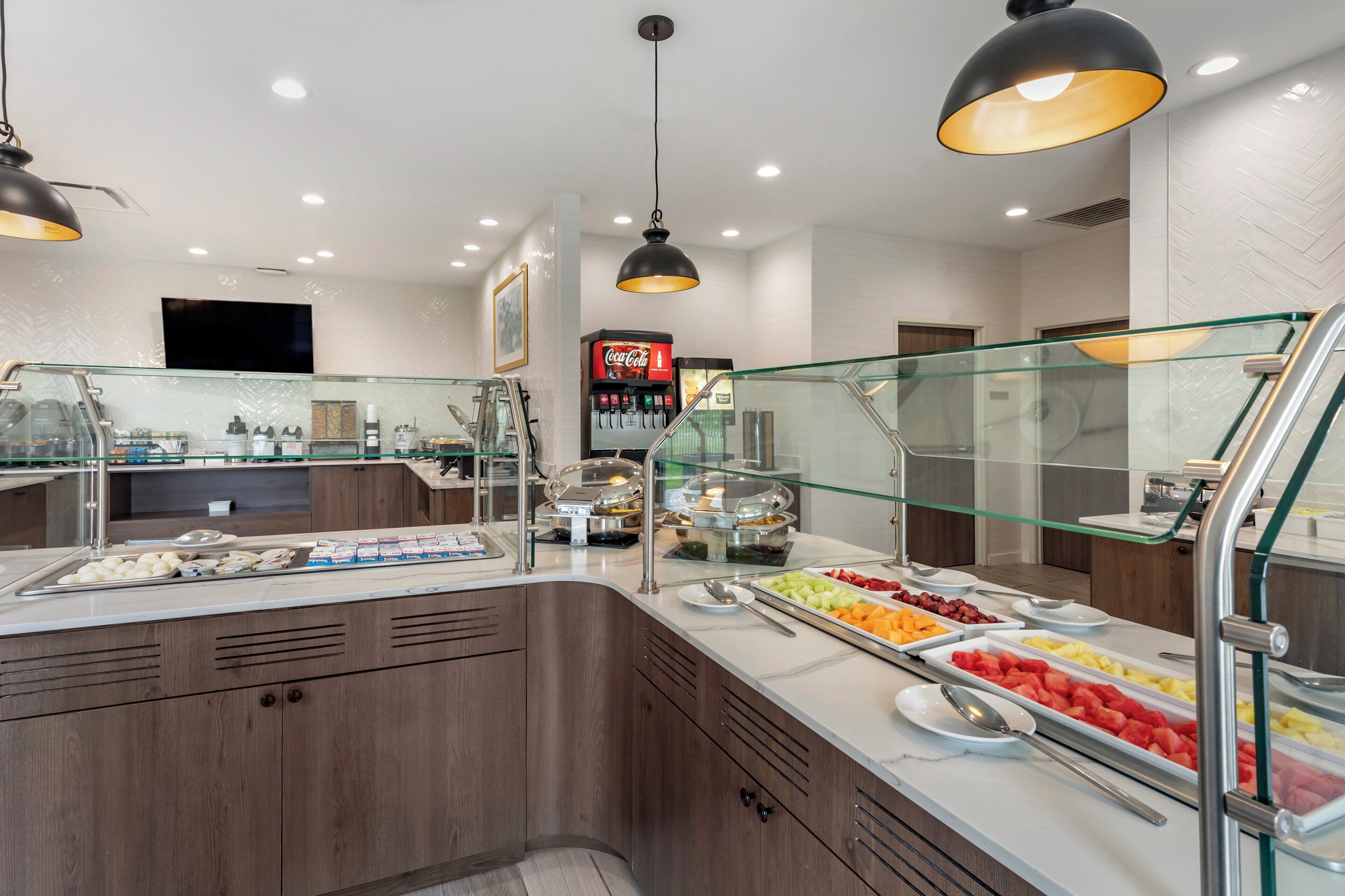 A buffet area with a variety of food options, a Coca-Cola refrigerator, and a glass railing.