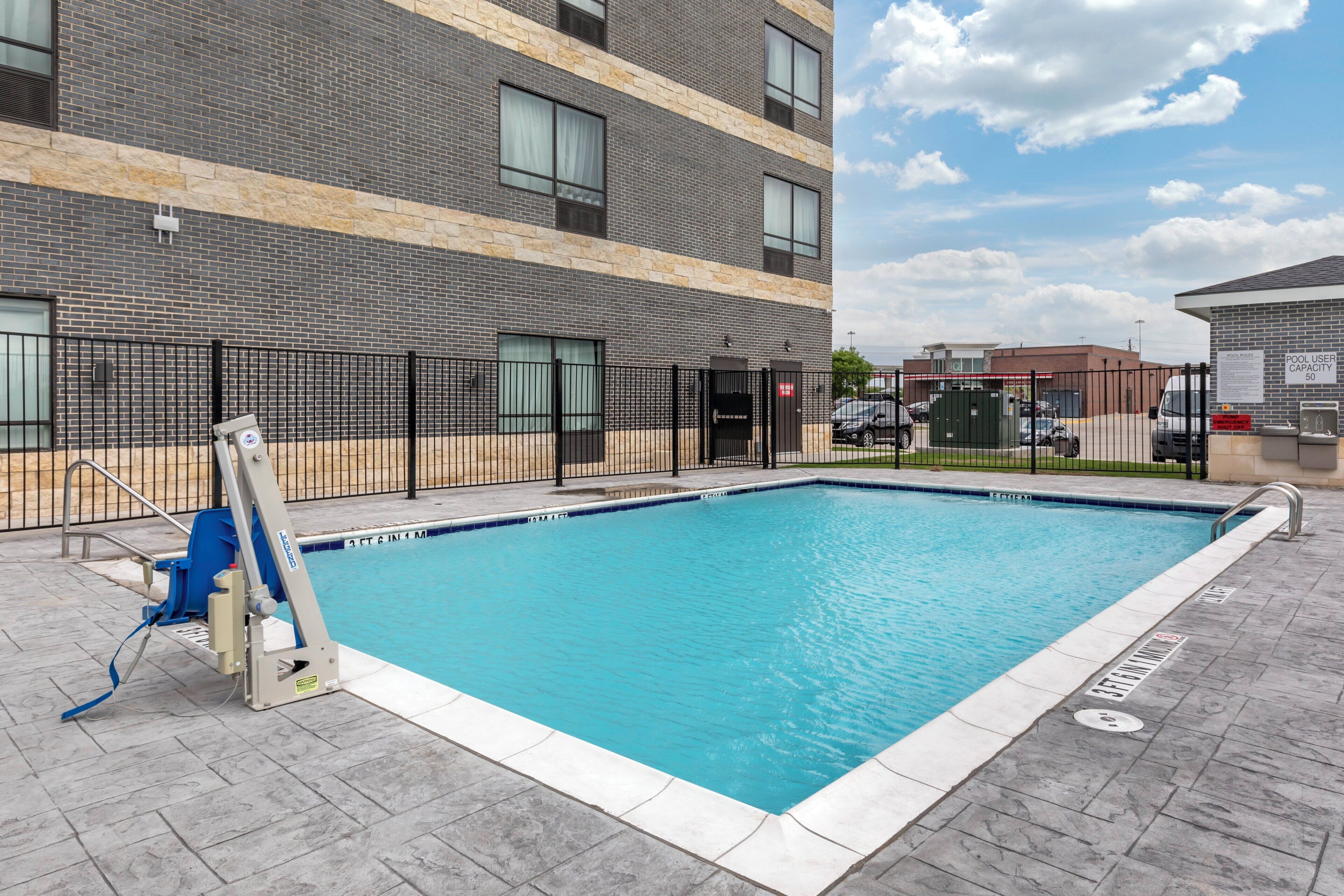 Una piscina con una silla de salvavidas y una valla, rodeada por un edificio de fachada de ladrillo.