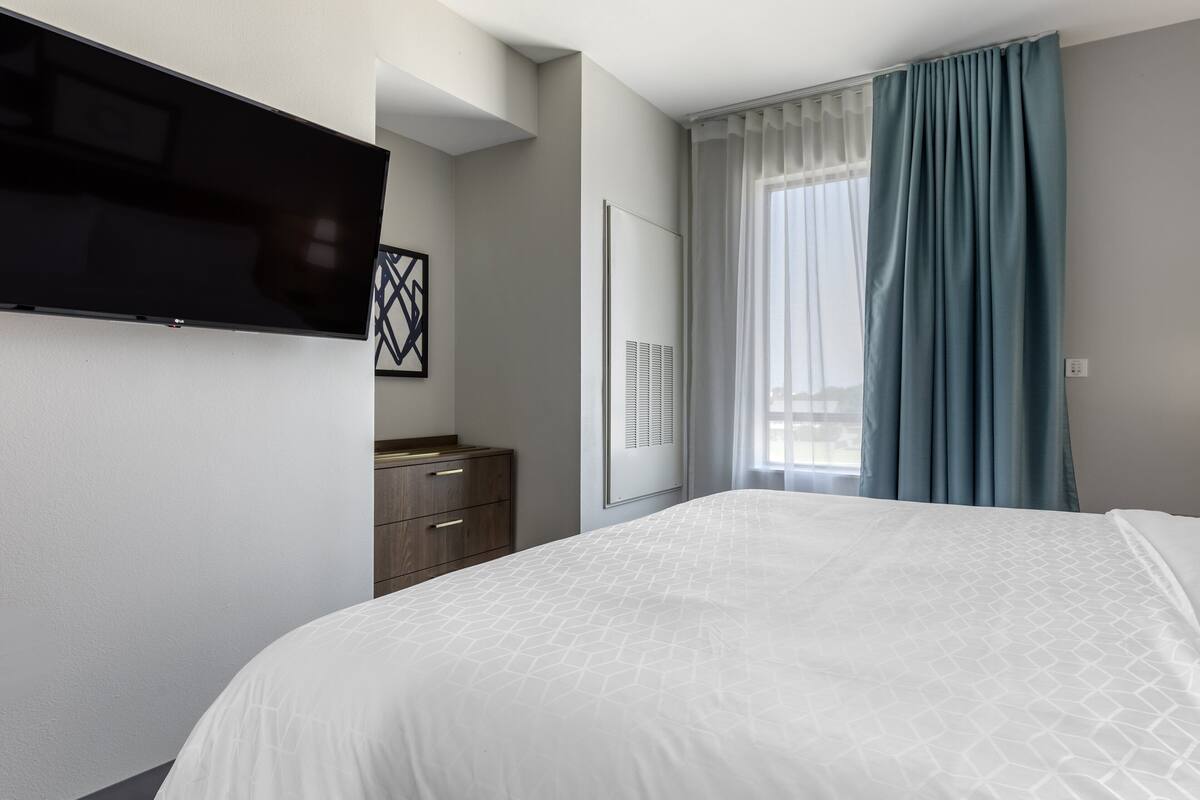 A hotel room with a large bed, a flat-screen TV mounted on the wall, a wardrobe, and a window with curtains.