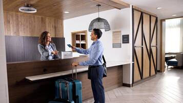 A hotel reception area with a wooden reception desk, a blue suitcase, and a person interacting with a receptionist.