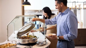 Un buffet proposant une variété de plats et une personne chargée de servir les aliments.