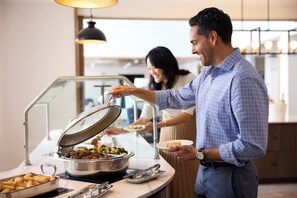 Un buffet proposant une variété de plats et une personne chargée de servir les aliments.