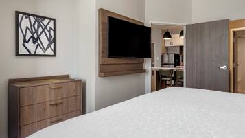 Une chambre d’hôtel comprenant un lit, une commode, un téléviseur à écran plat fixé au mur et un coin repas visible à travers une porte ouverte.