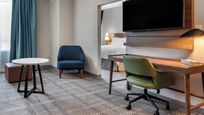 Une chambre d’hôtel comprenant un lit, un téléviseur fixé au mur, un bureau avec une chaise, une petite table ronde et un canapé.