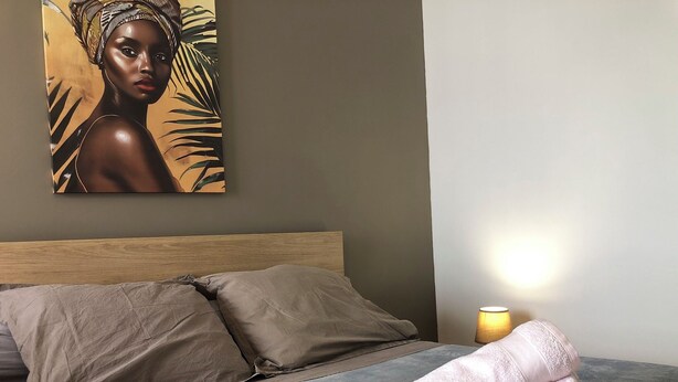 A neatly made bed with beige pillows and a folded towel on a grey mattress.
