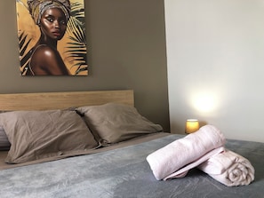 Ein ordentlich bezogenes Bett mit beigen Kissen und einem gefalteten Handtuch auf einer grauen Matratze.