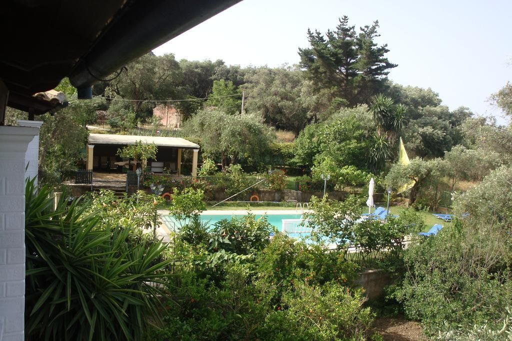 A pool area surrounded by lush greenery, with a covered seating area and a building in the background.