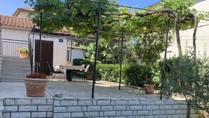 Un patio con escalones de piedra que conducen a una mesa y sillas, rodeado de vegetación y una pérgola.
