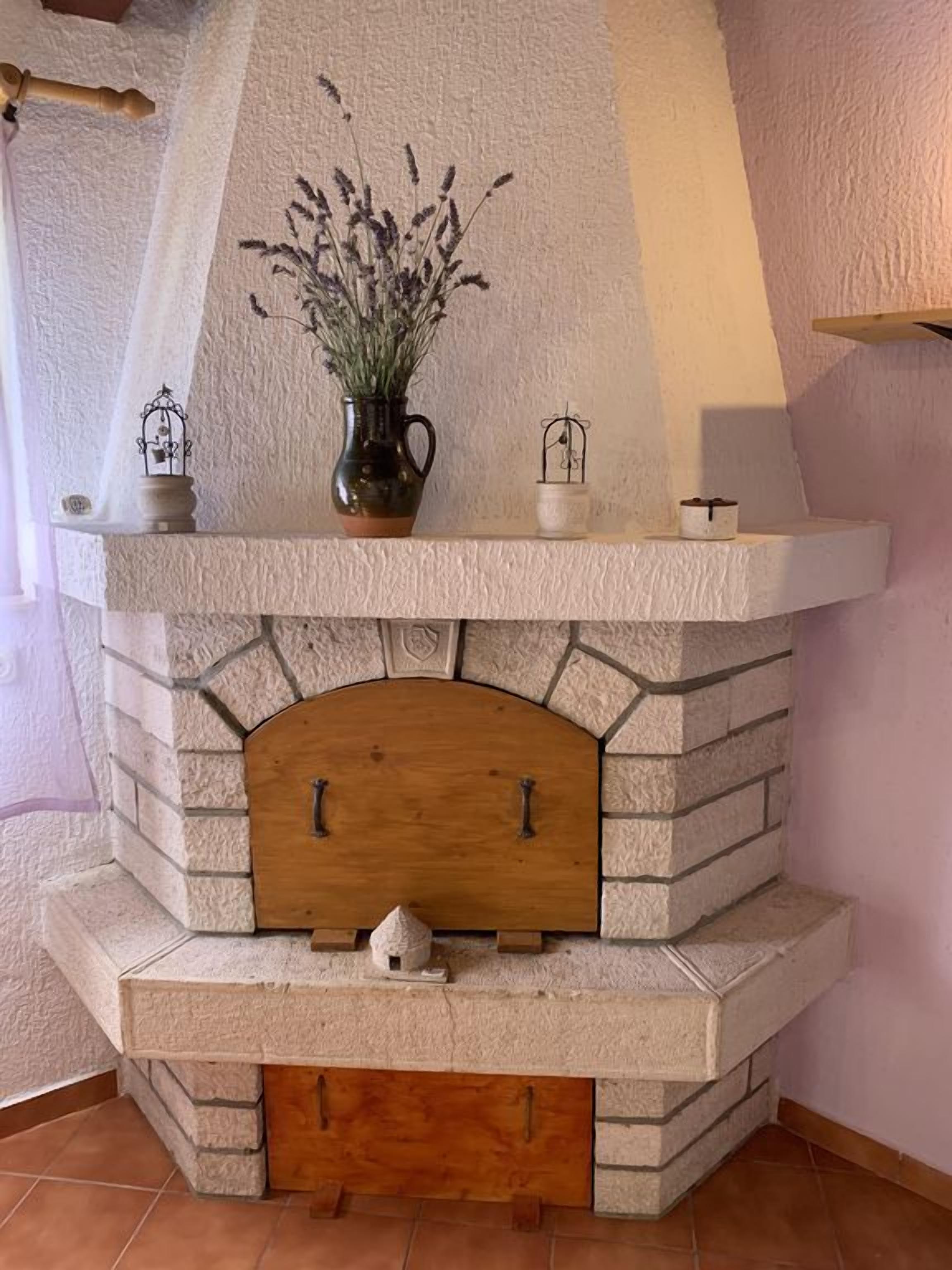 Une cheminée en pierre surmontée d’une arche en bois, un vase avec des plantes et deux petites cages à oiseaux posées sur le manteau de la cheminée.