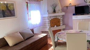 Una sala de estar acogedora con un sofá, una mesa de comedor con sillas, una chimenea y un televisor.