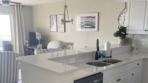 Una cocina moderna con armarios blancos, lavavajillas empotrado, un lavabo y una ventana con cortinas.
