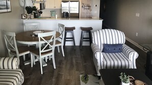 Una cocina moderna con armarios blancos, un refrigerador de acero inoxidable y una isla de madera. Hay una mesa de comedor con sillas y un sillón a rayas.