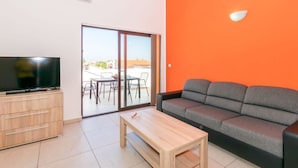 A modern living room with a television, a sofa, a coffee table, and a sliding glass door leading to an outdoor area. - Apartment Janko N1 (Medulin)