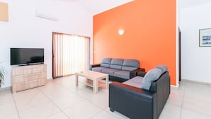 A modern living room with a large orange accent wall, a flat-screen TV, a wooden coffee table, and a black sofa. - Apartment Janko N1 (Medulin)