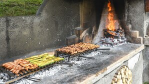 Una parrilla con diversos tipos de carne y verduras asándose sobre fuego abierto.