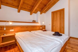A wooden bedroom with a bed, bedside lamps, and a wooden wardrobe.