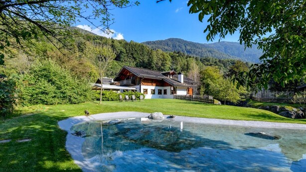 Una casa con piscina rodeada de un césped cuidado y un paisaje boscoso en la colina.