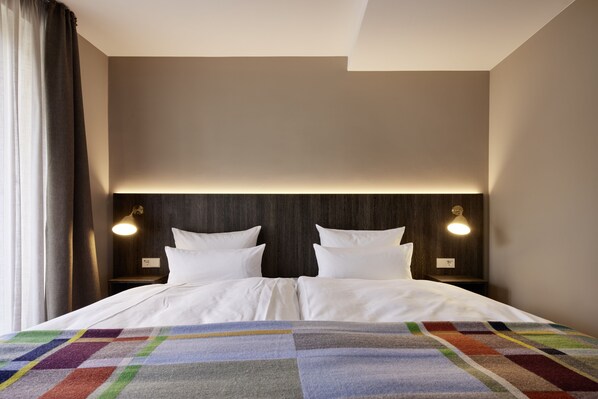 A neatly made bed with white linens and a colorful blanket, two bedside tables with lamps, and a dark wooden headboard. - Central Hotel Münster (Münster)