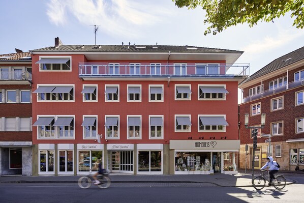 A multi-story building with a red facade, storefronts on the ground floor, and a balcony on the second floor. - Central Hotel Münster (Münster)