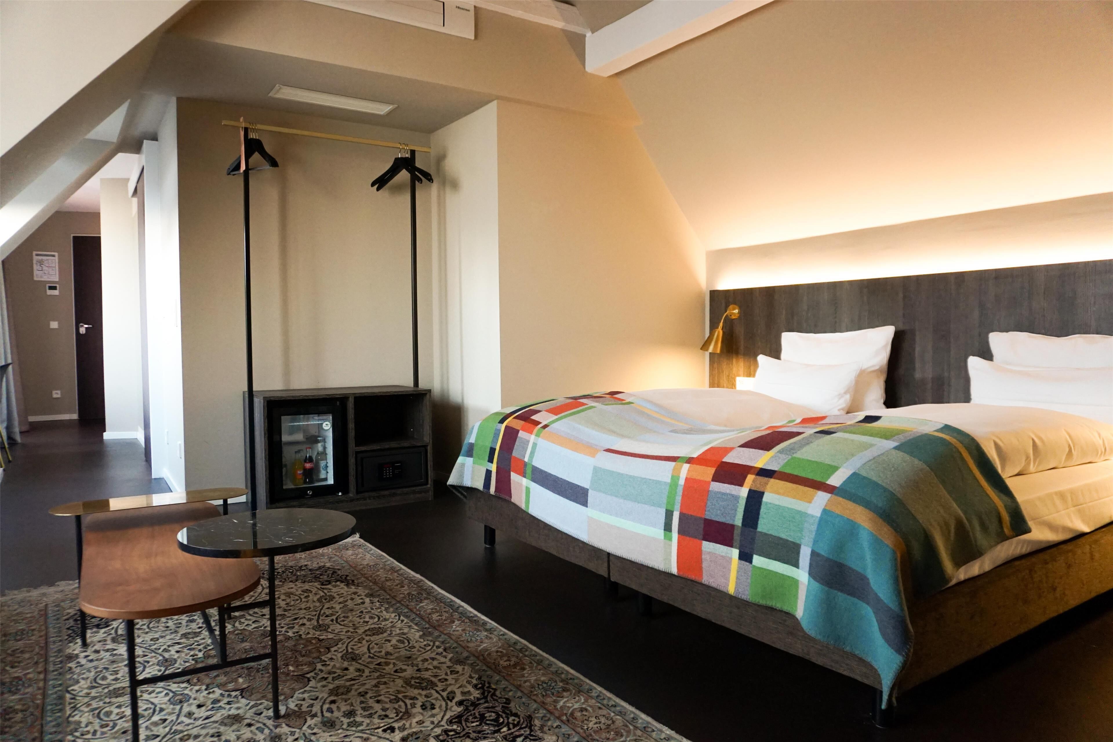 Une chambre d’hôtel moderne avec un grand lit, une petite table, un canapé, une cheminée et un luminaire suspendu.