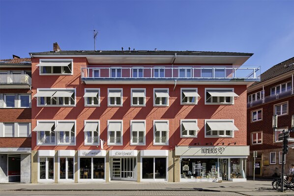 A multi-story building with a red facade, multiple balconies, and storefronts including 'Edelweiss' and 'Homeweis'. - Central Hotel Münster (Münster)