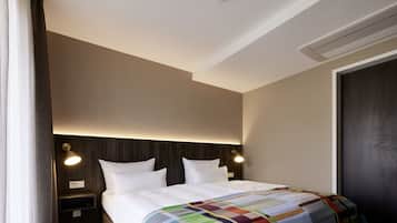 Une chambre d’hôtel dotée d’un grand lit, de deux tables de chevet, d’une tête de lit avec éclairage intégré, d’un détecteur de fumée fixé au plafond et d’une porte avec un panneau sombre.