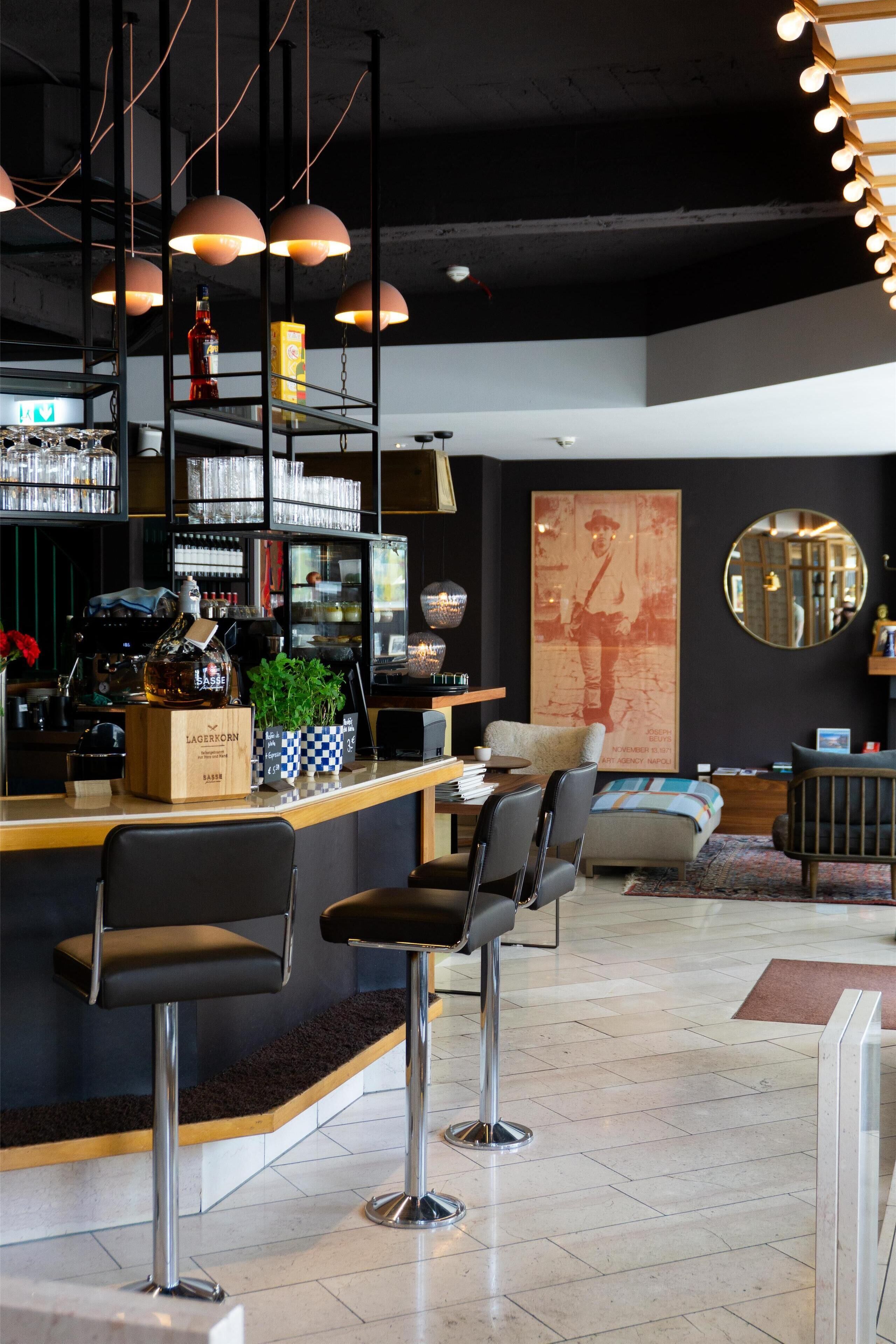 Een moderne bar met krukken, planken vol flessen en een grote poster aan de muur.