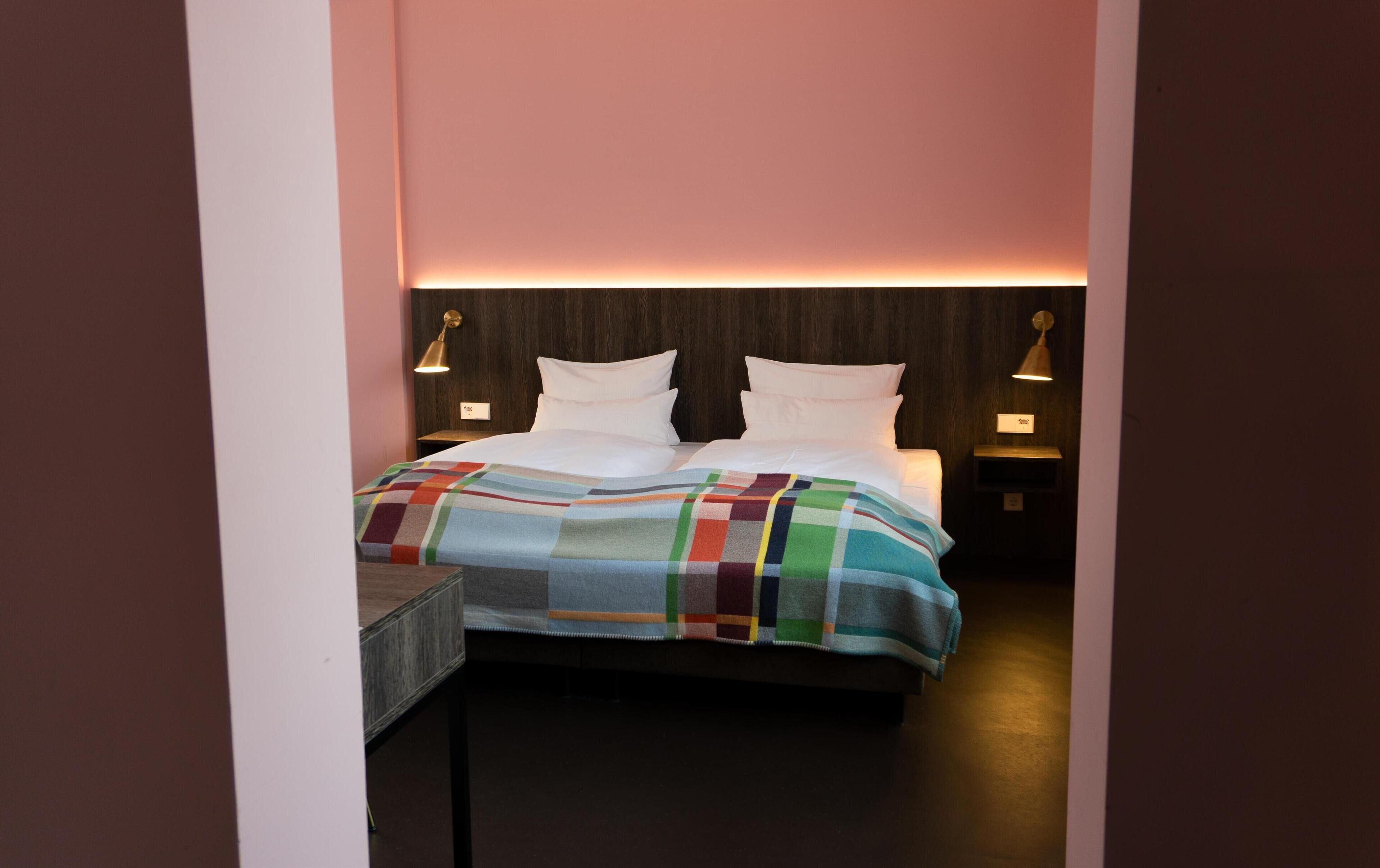 A neatly made bed with a colorful blanket, two bedside lamps, and a dark headboard.