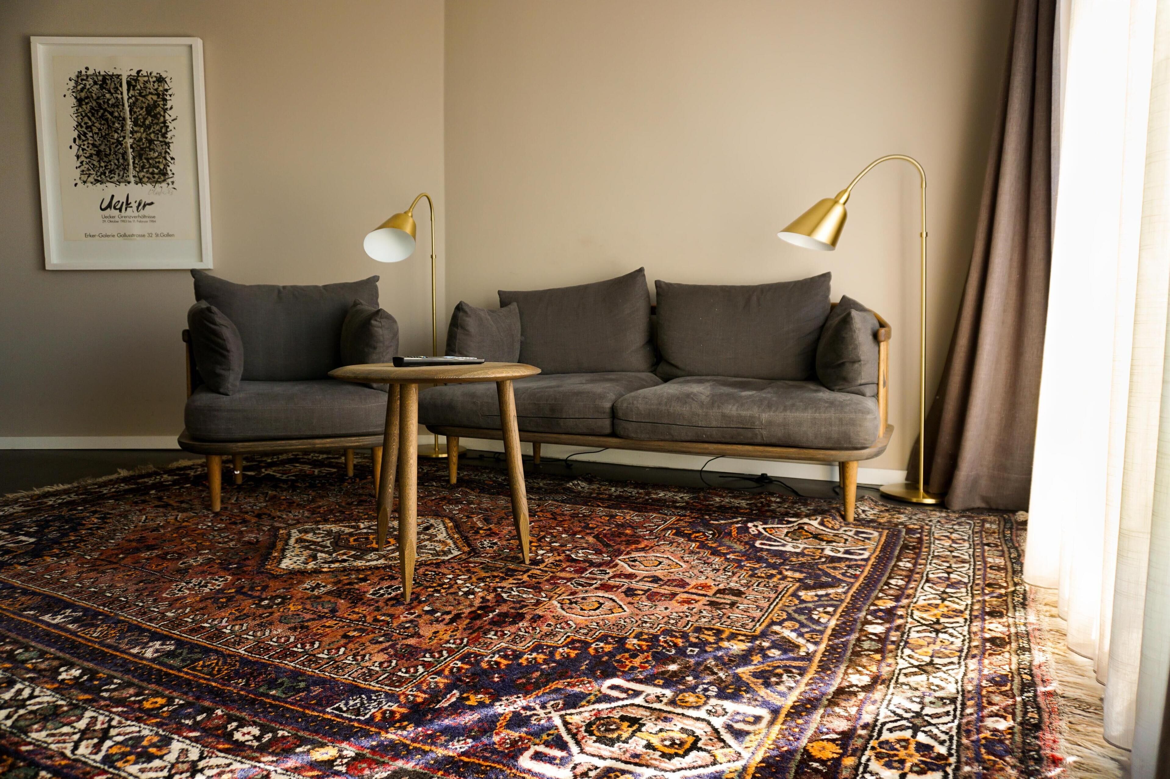 A modern living room with a grey sofa, a round wooden coffee table, and a patterned rug.
