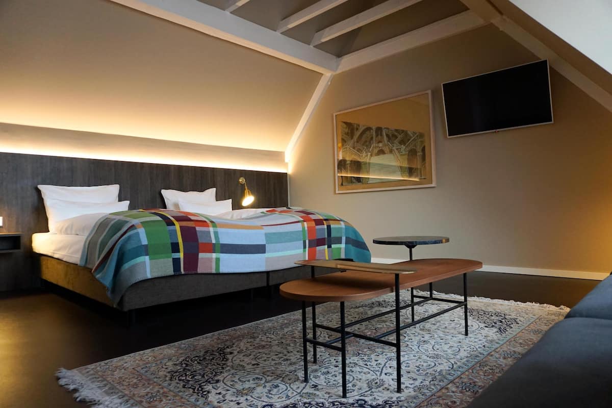 A bedroom with a bed, bedside tables, a small table, a chair, a TV, and a patterned rug.