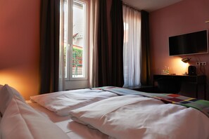 A hotel room with a bed, a desk, a chair, a TV, and a window with curtains. - Central Hotel Münster (Münster)